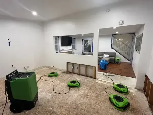 Dehumidifier and air movers drying a stripped floor in a finished lower level